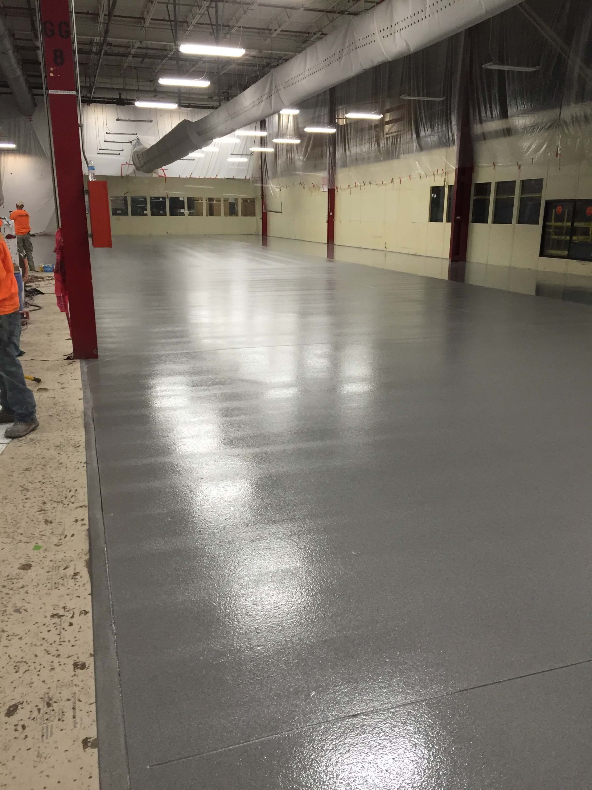 A large empty room with a gray floor and a few people standing around it.