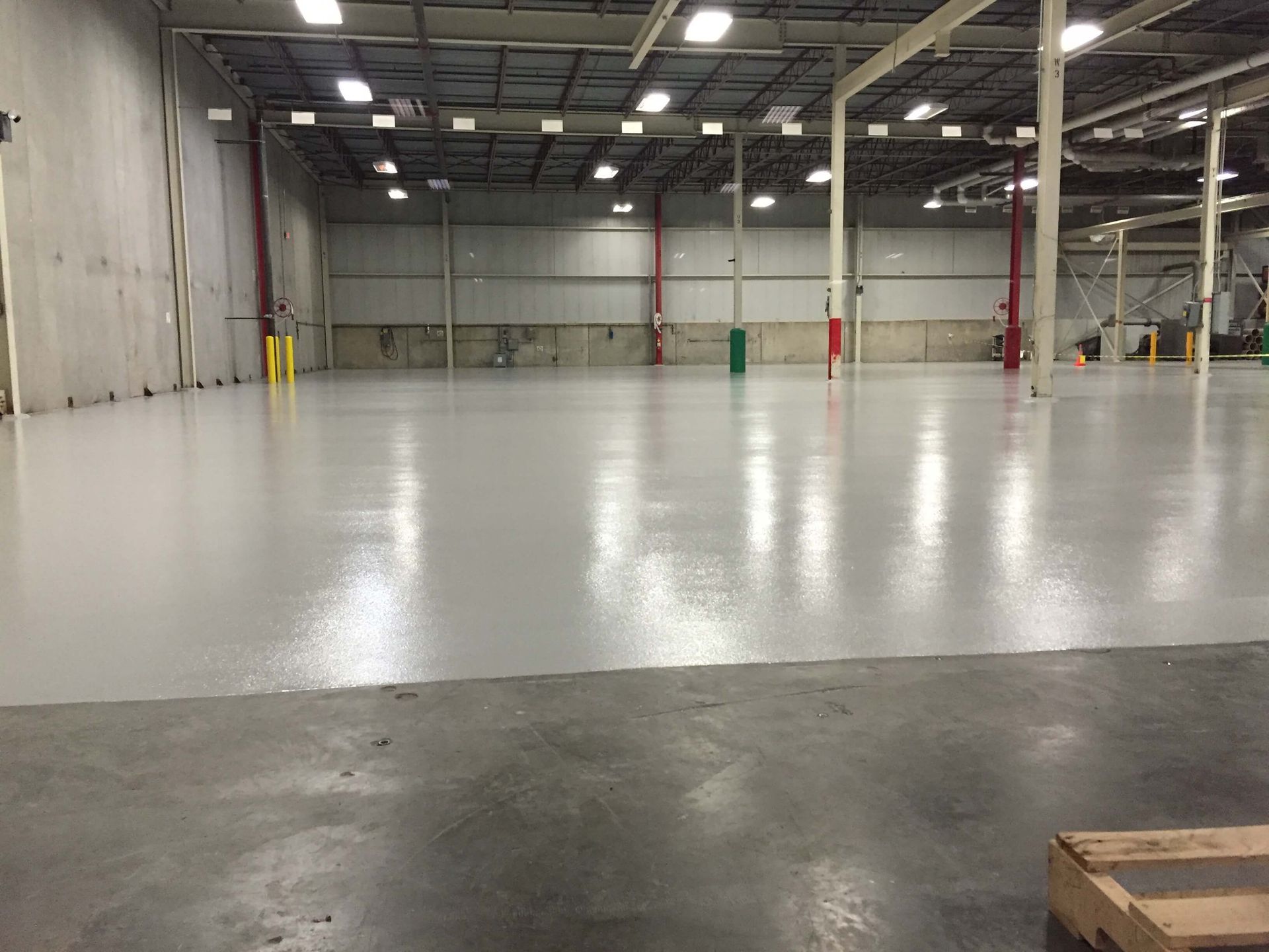 A large warehouse with a concrete floor and a wooden pallet in the foreground.