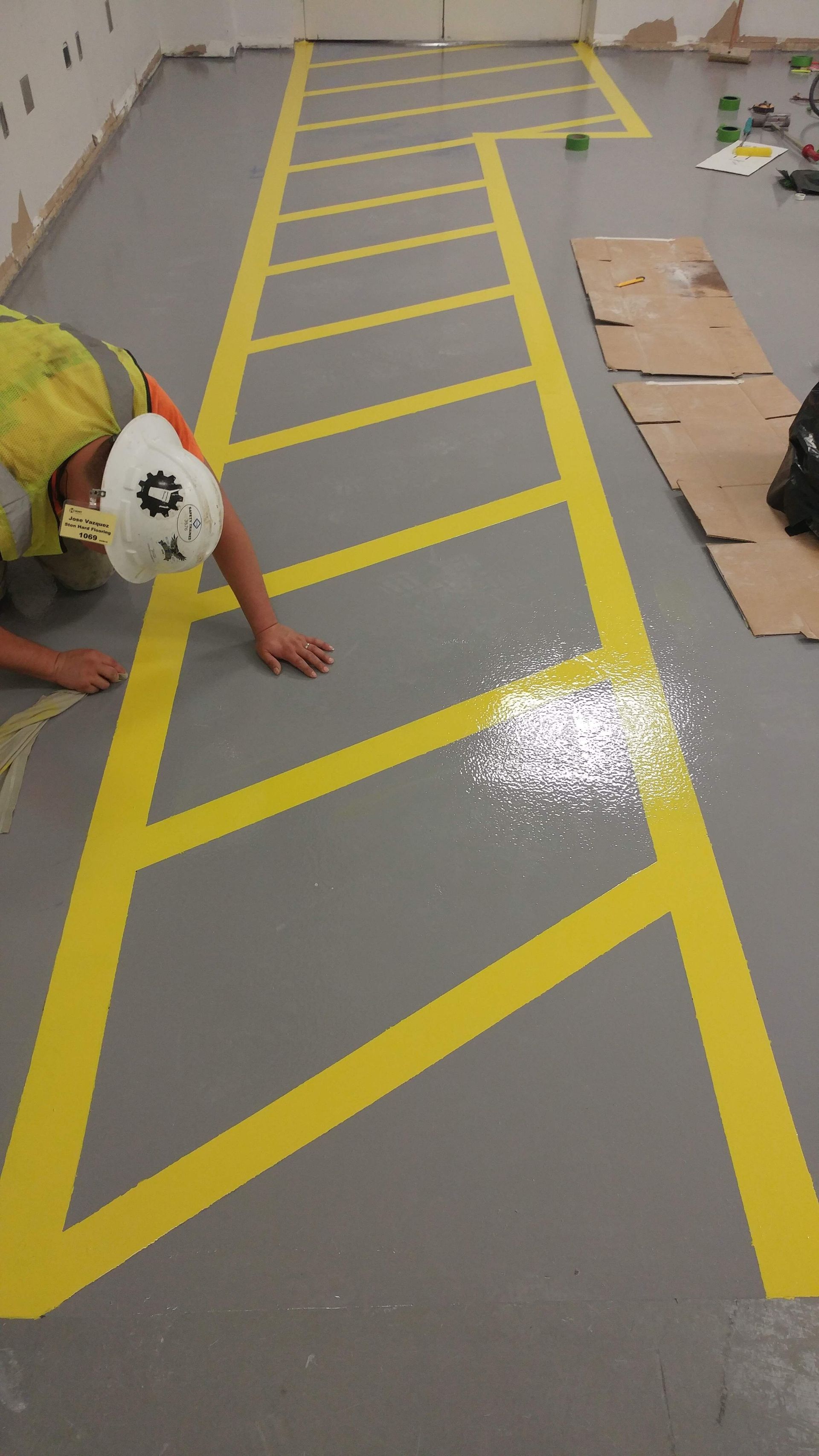 A man is kneeling on the floor painting a yellow line on the floor.