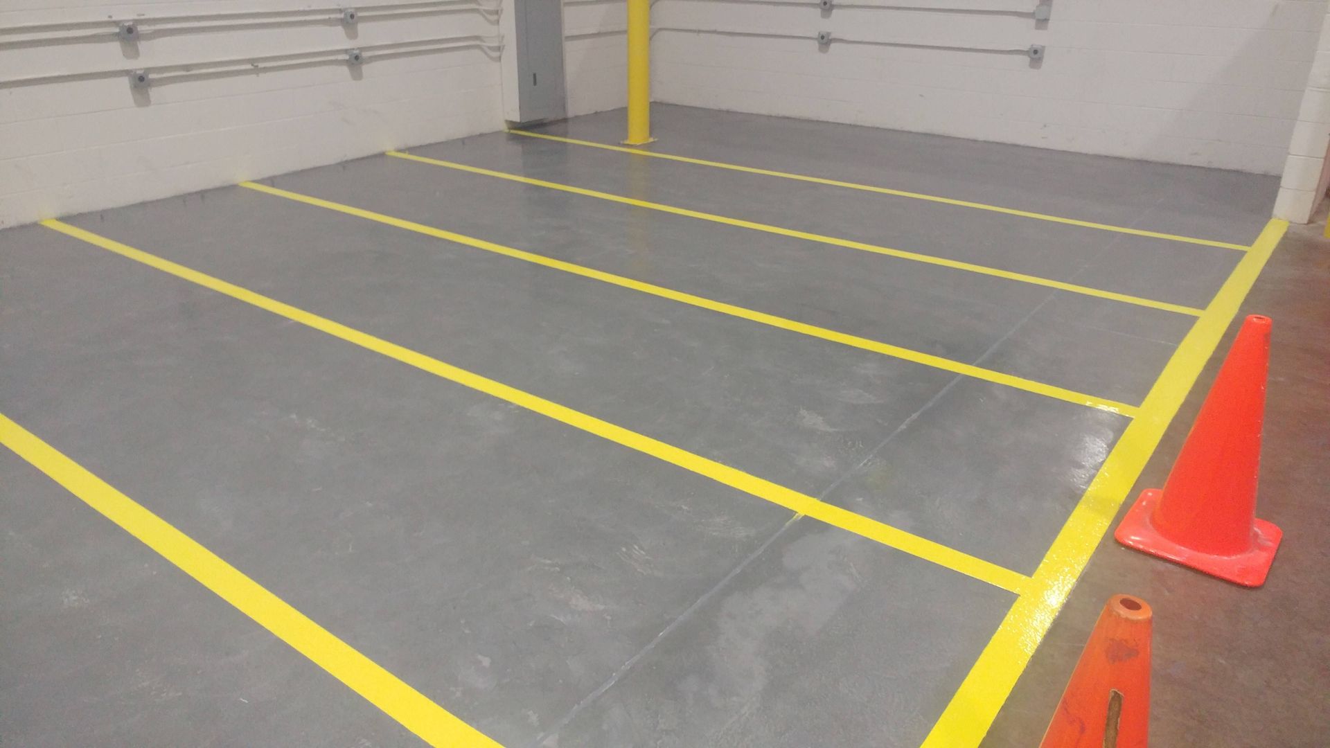 A parking lot with yellow lines on the floor and orange cones.