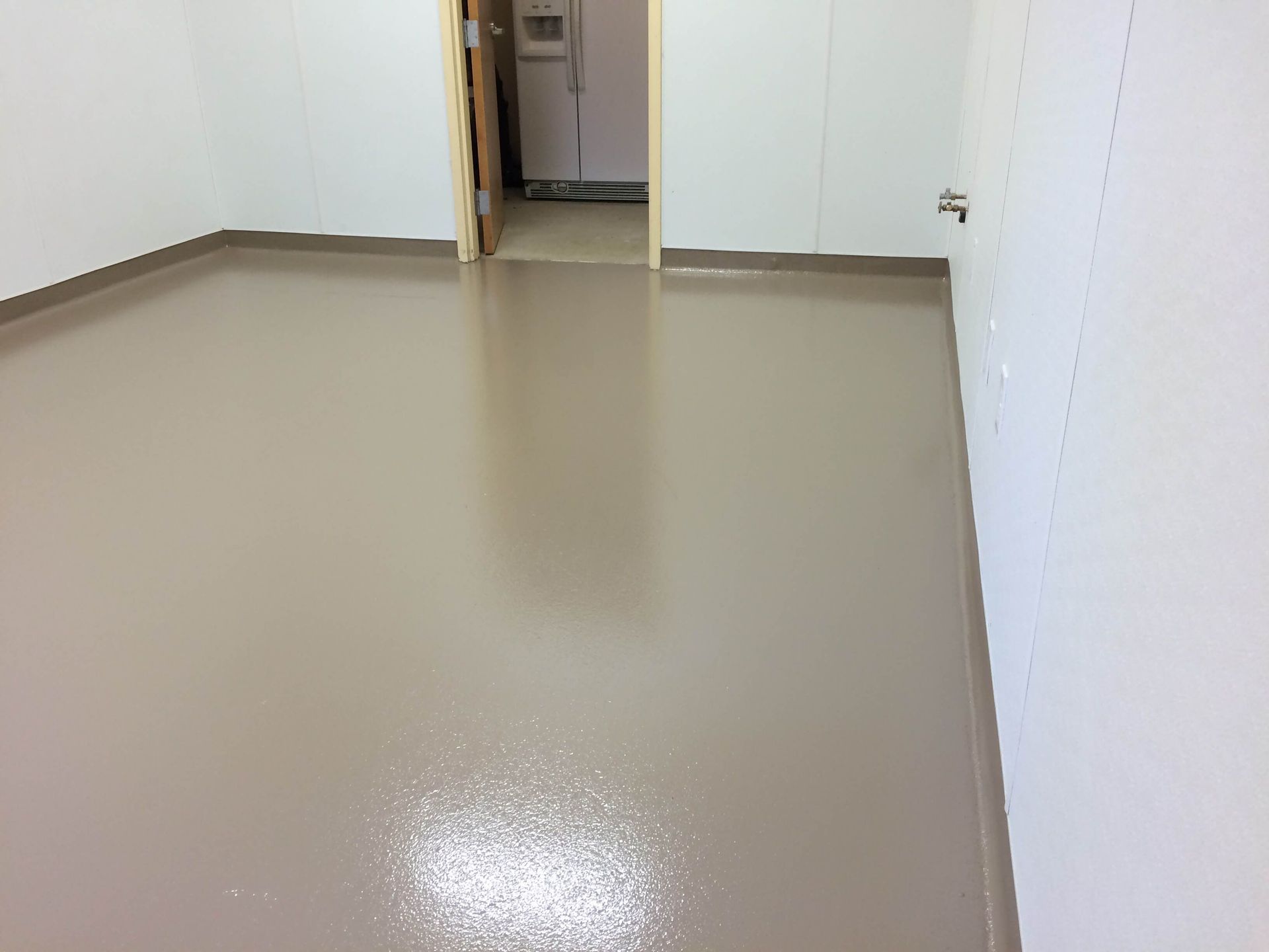 A small, empty room with a smooth, tan-colored floor and white walls. A doorway is visible.