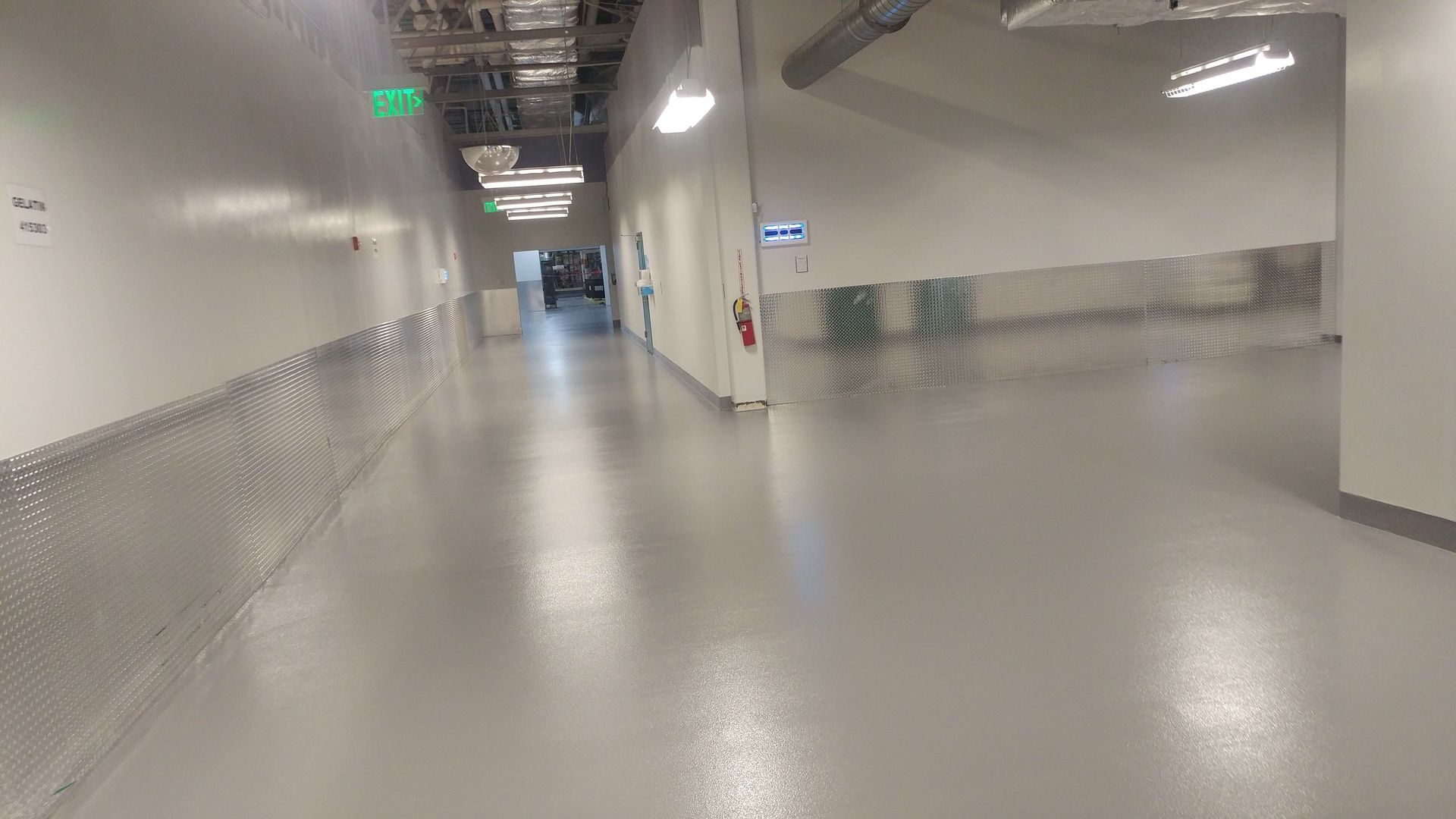 Hallway with shiny gray floor, white walls, and fluorescent lights.