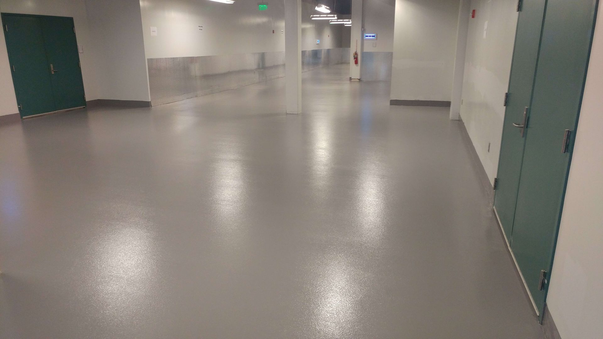 Hallway with gray floor, green doors, white walls.