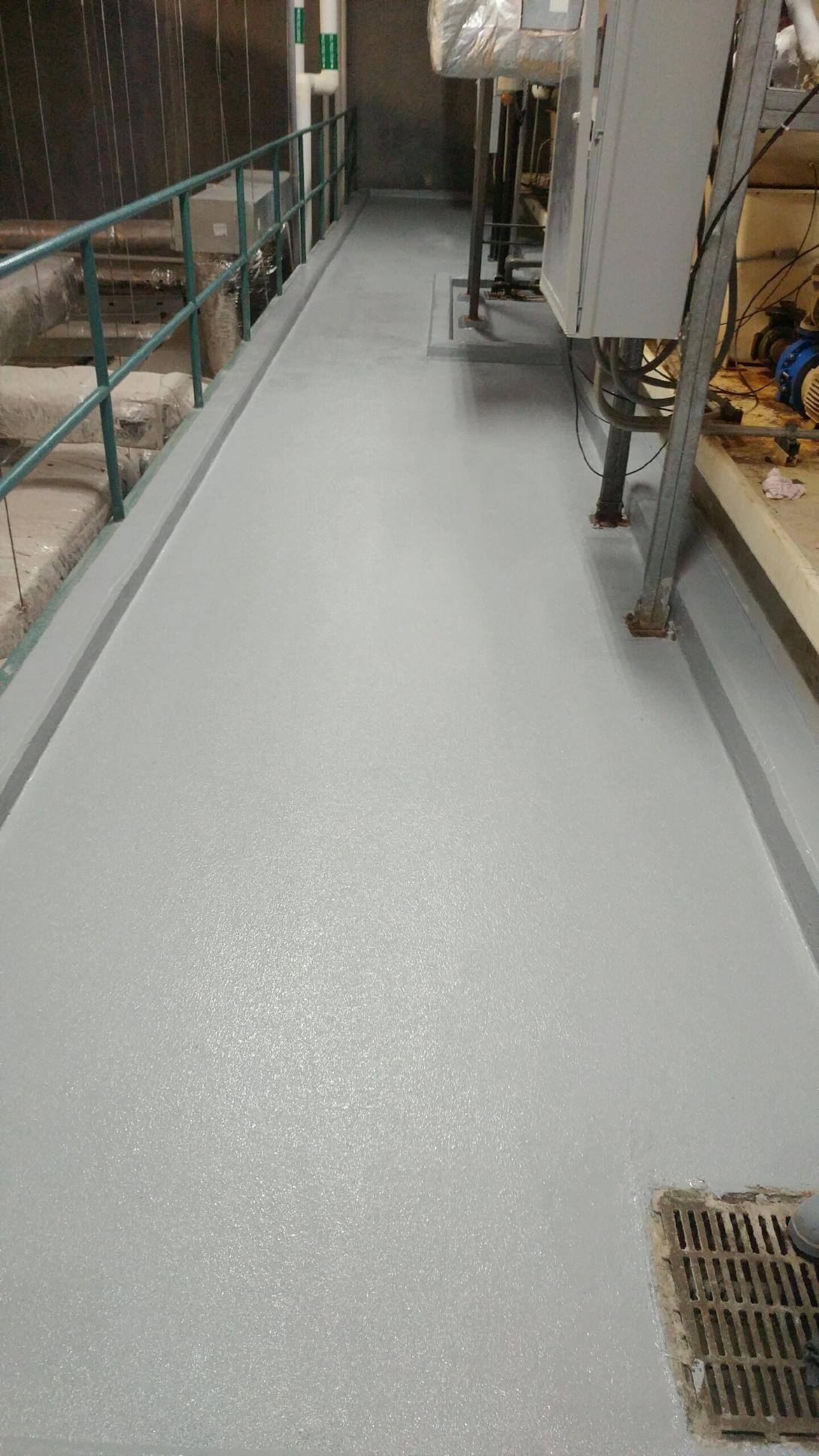 Gray industrial walkway with handrail on left and machinery on right.