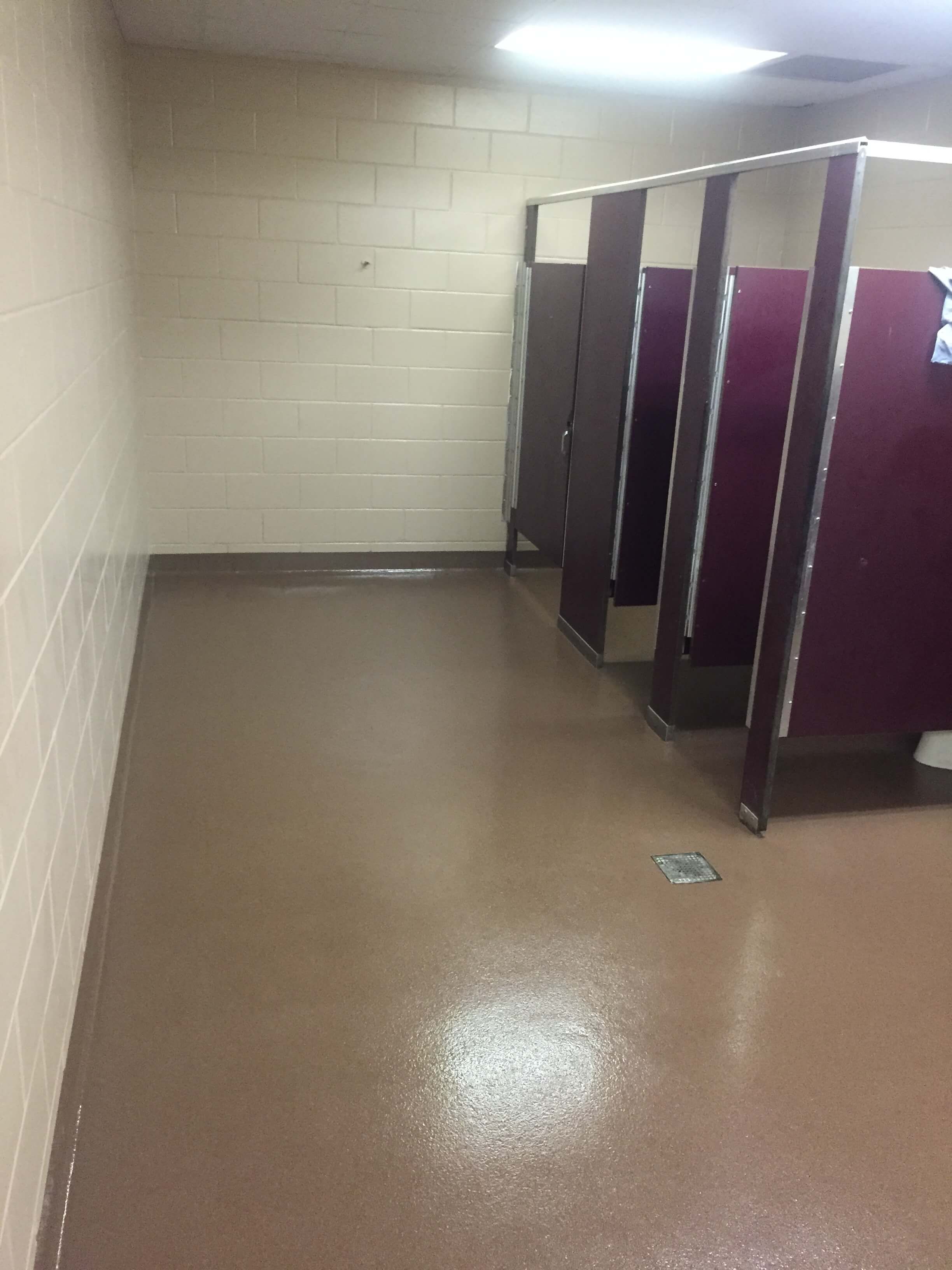 Public restroom with brown floor, beige walls, and maroon stall doors.