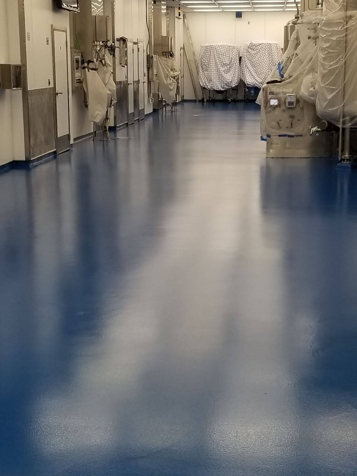 Blue, glossy industrial floor in a factory setting. Machinery and equipment line the walls.