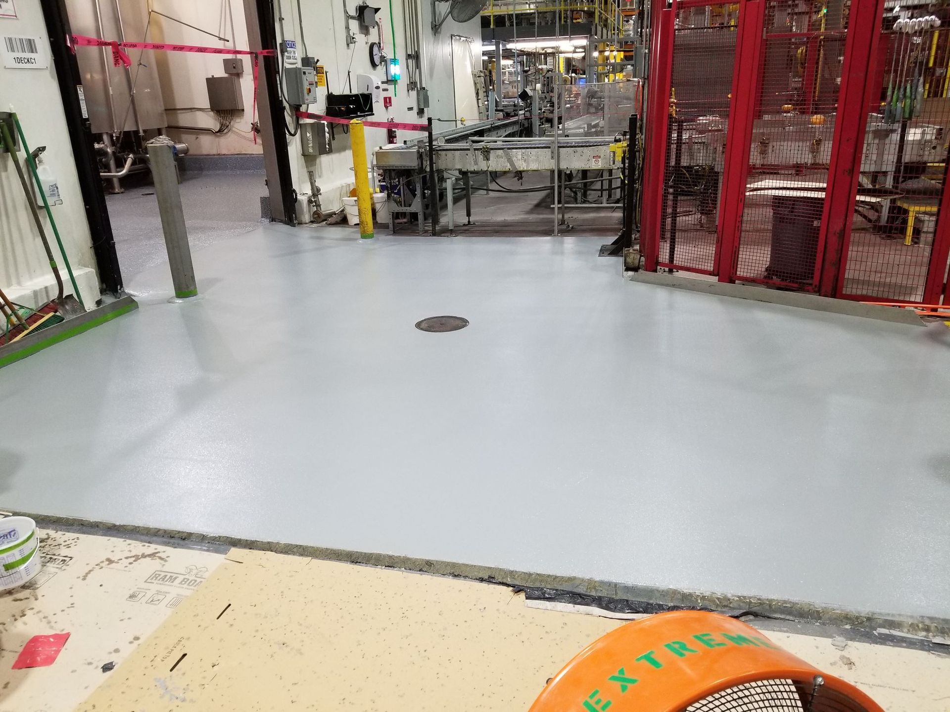 A room with a gray floor and a red fence in a factory.