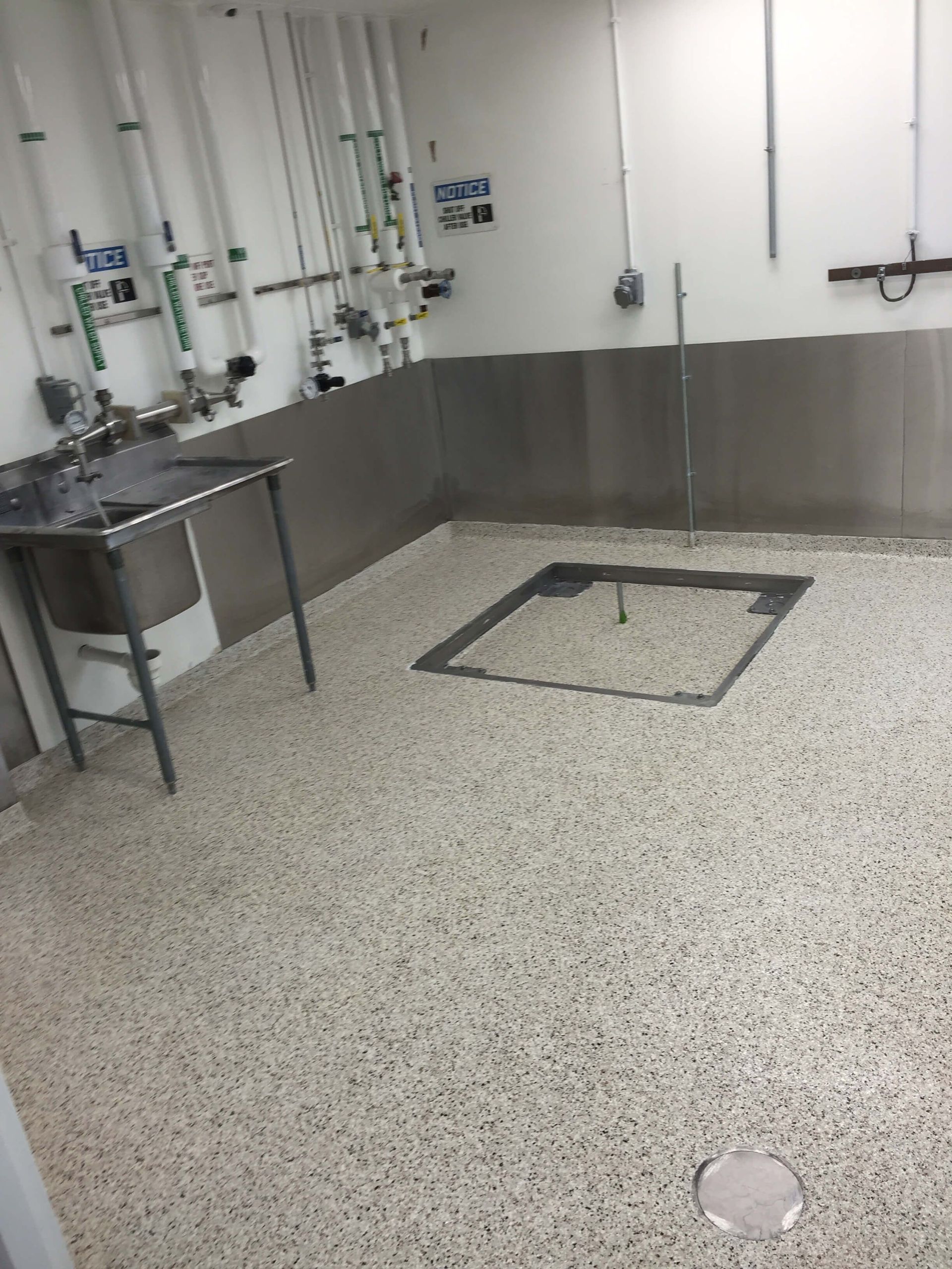 Clean, industrial room with stainless steel walls, sink, and speckled flooring, possibly a lab.