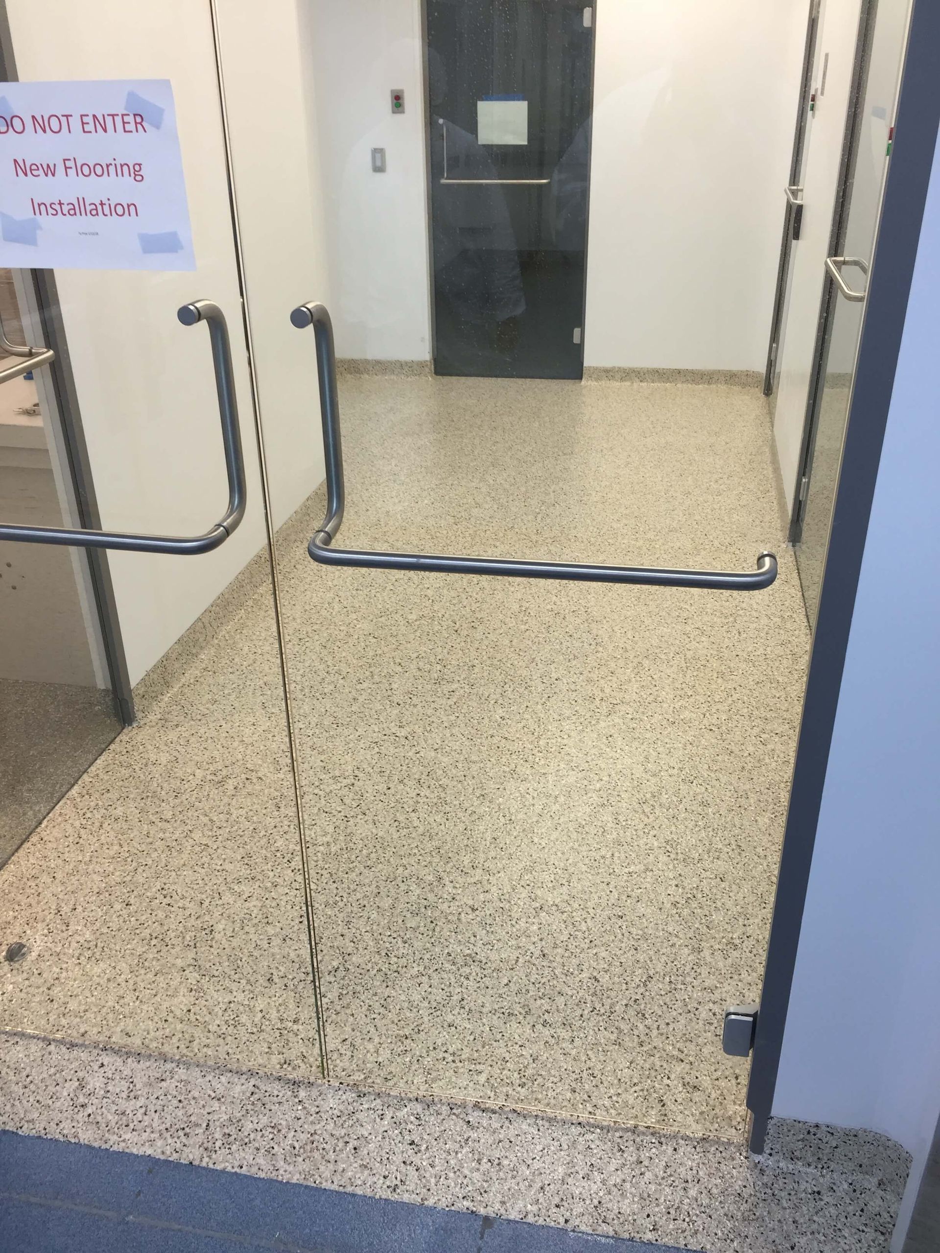 Hallway with speckled floor, glass doors with handles, and a sign saying 