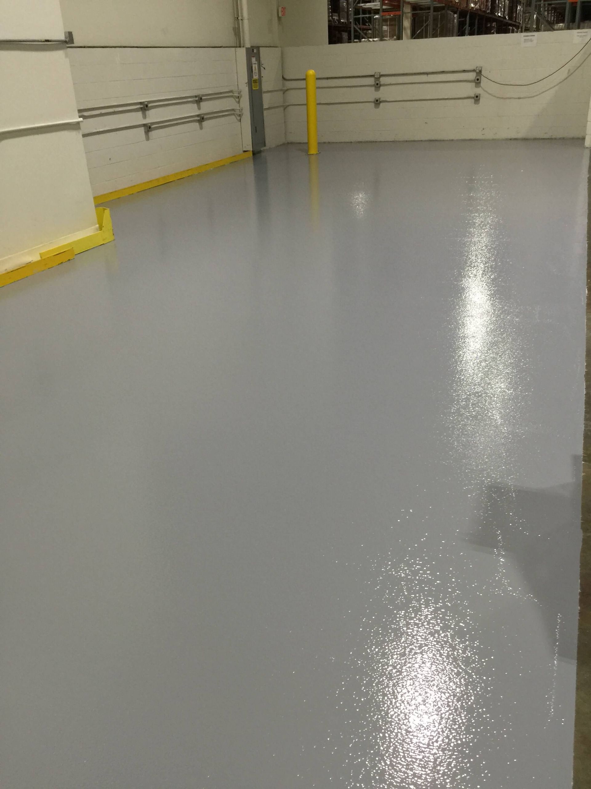 A shiny, gray epoxy floor in a warehouse with yellow safety markings and railings.