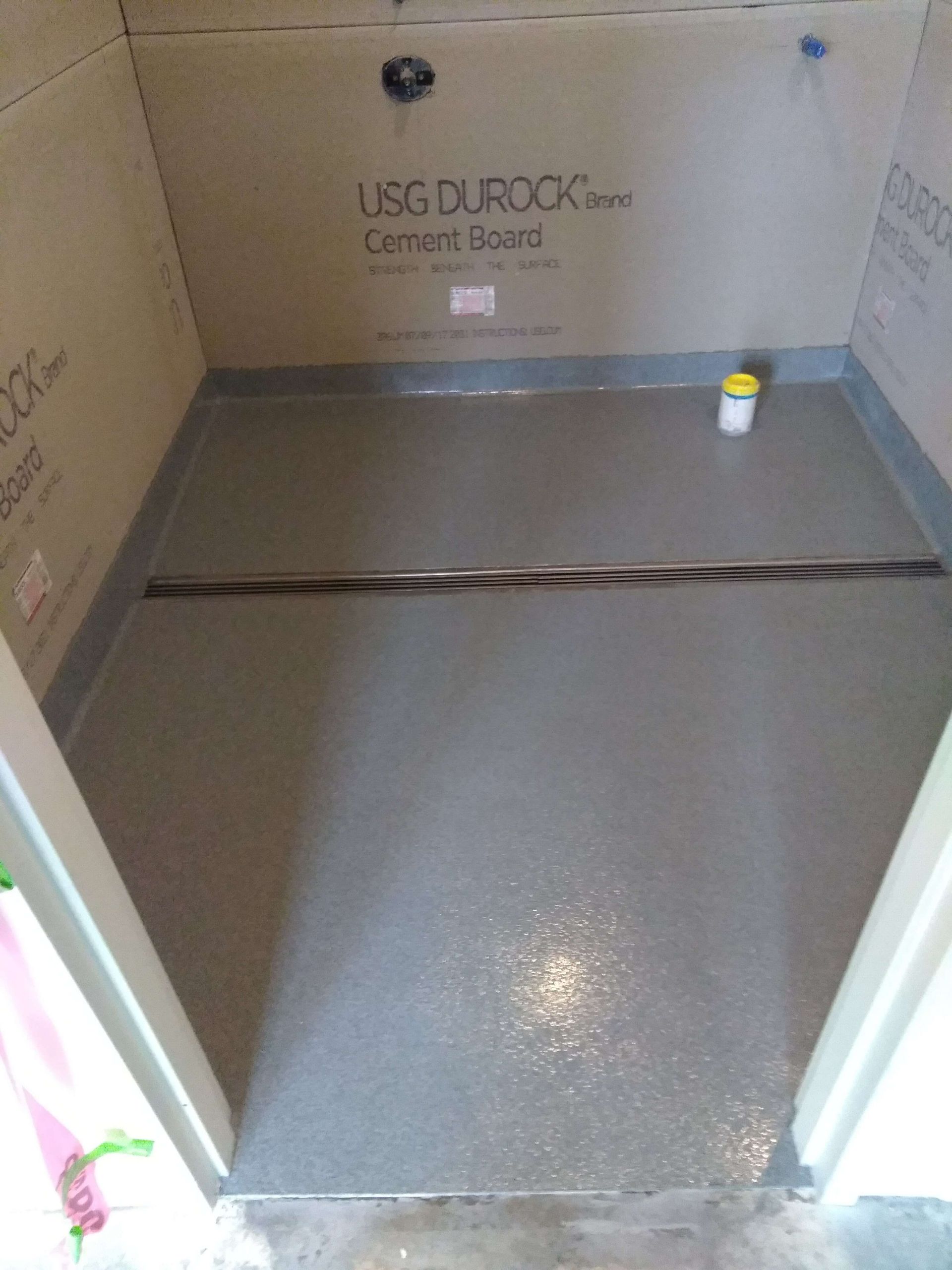 Cement shower floor, gray, with black drain line. Cement board walls.
