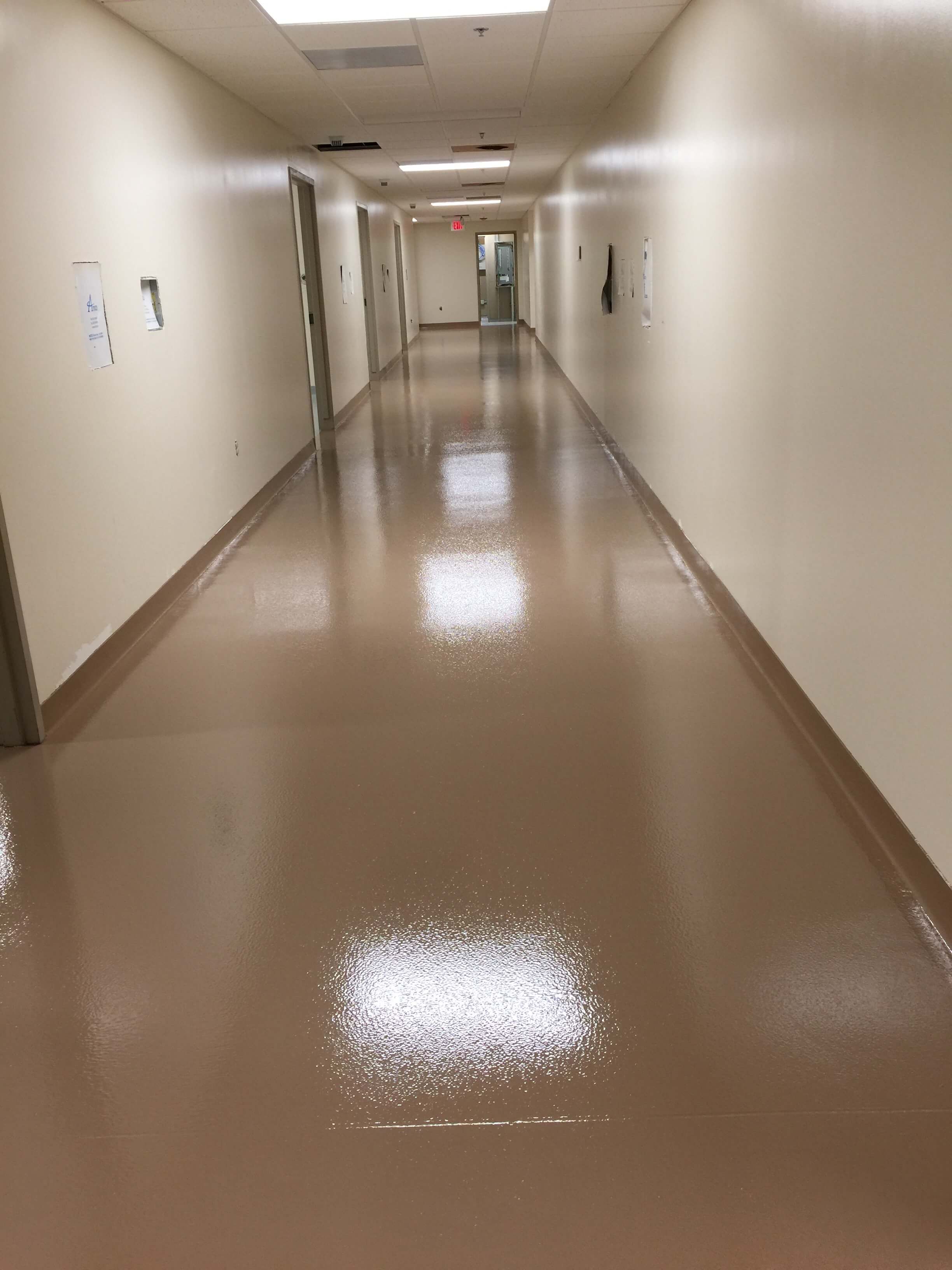 Long, shiny beige hallway with white walls and closed doors. Light reflects on the wet floor.
