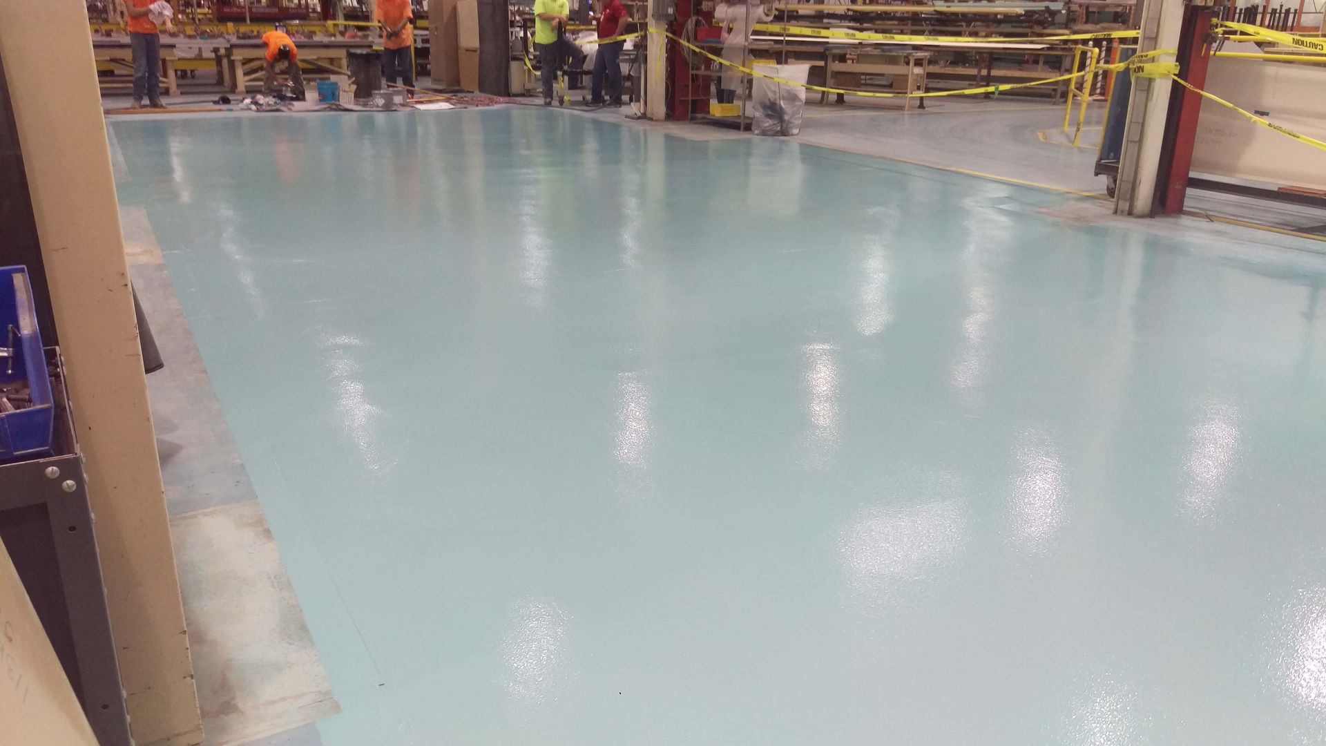 Light blue epoxy floor in a warehouse, workers in background.