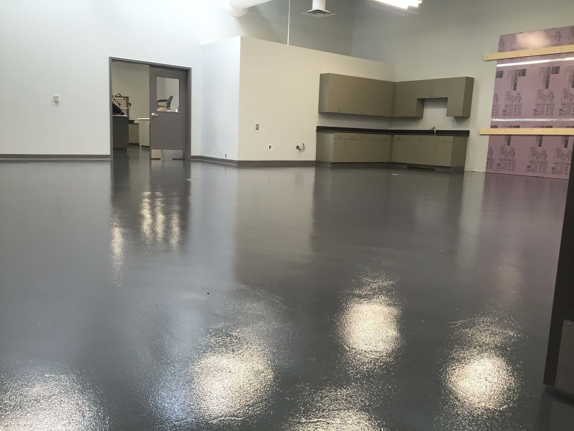 A gray epoxy-floored room with white walls, cabinetry, and a doorway leading to another room.