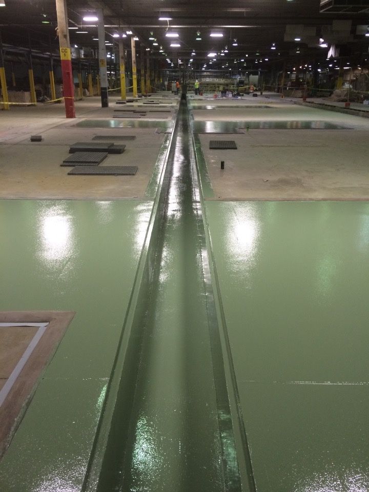 A large warehouse with a green floor and a drain in the middle.