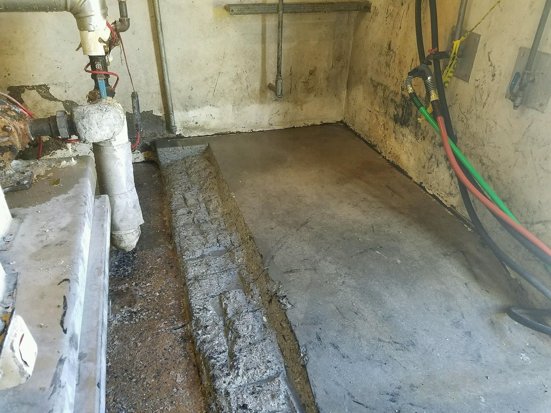 A dirty room with a lot of pipes and wires.