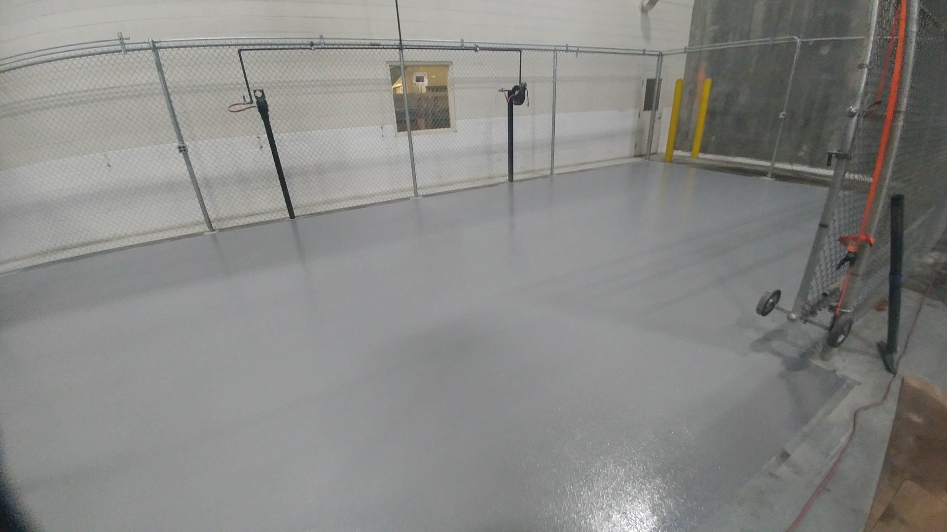 A gray concrete floor in a room with a fence and a ladder.