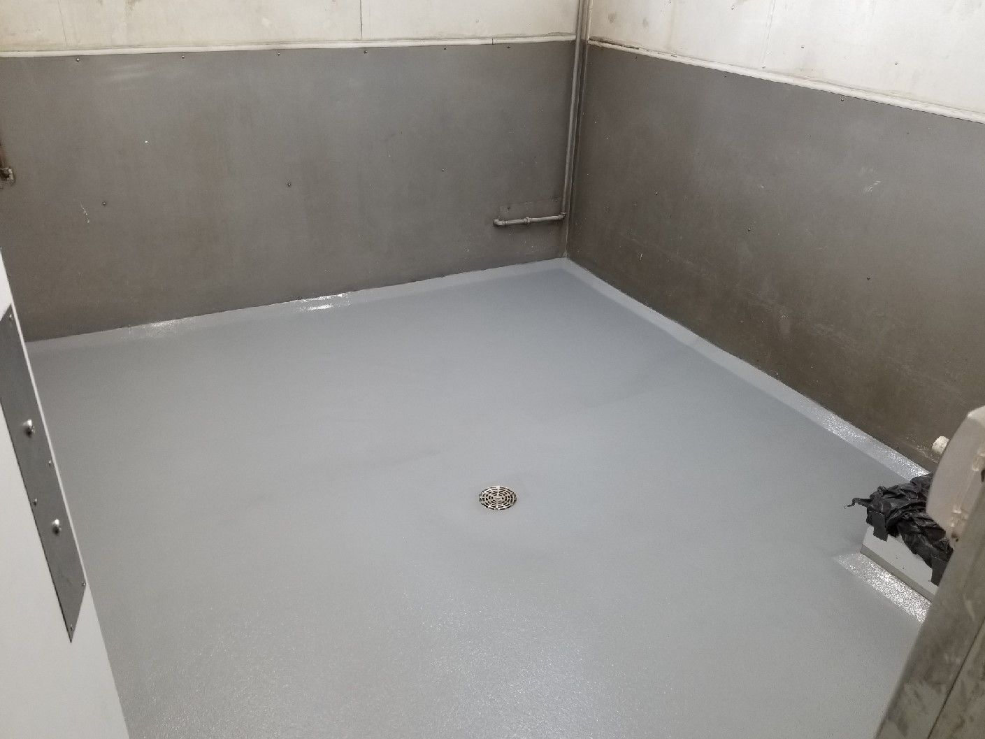 A room with a gray floor and a drain on the floor.