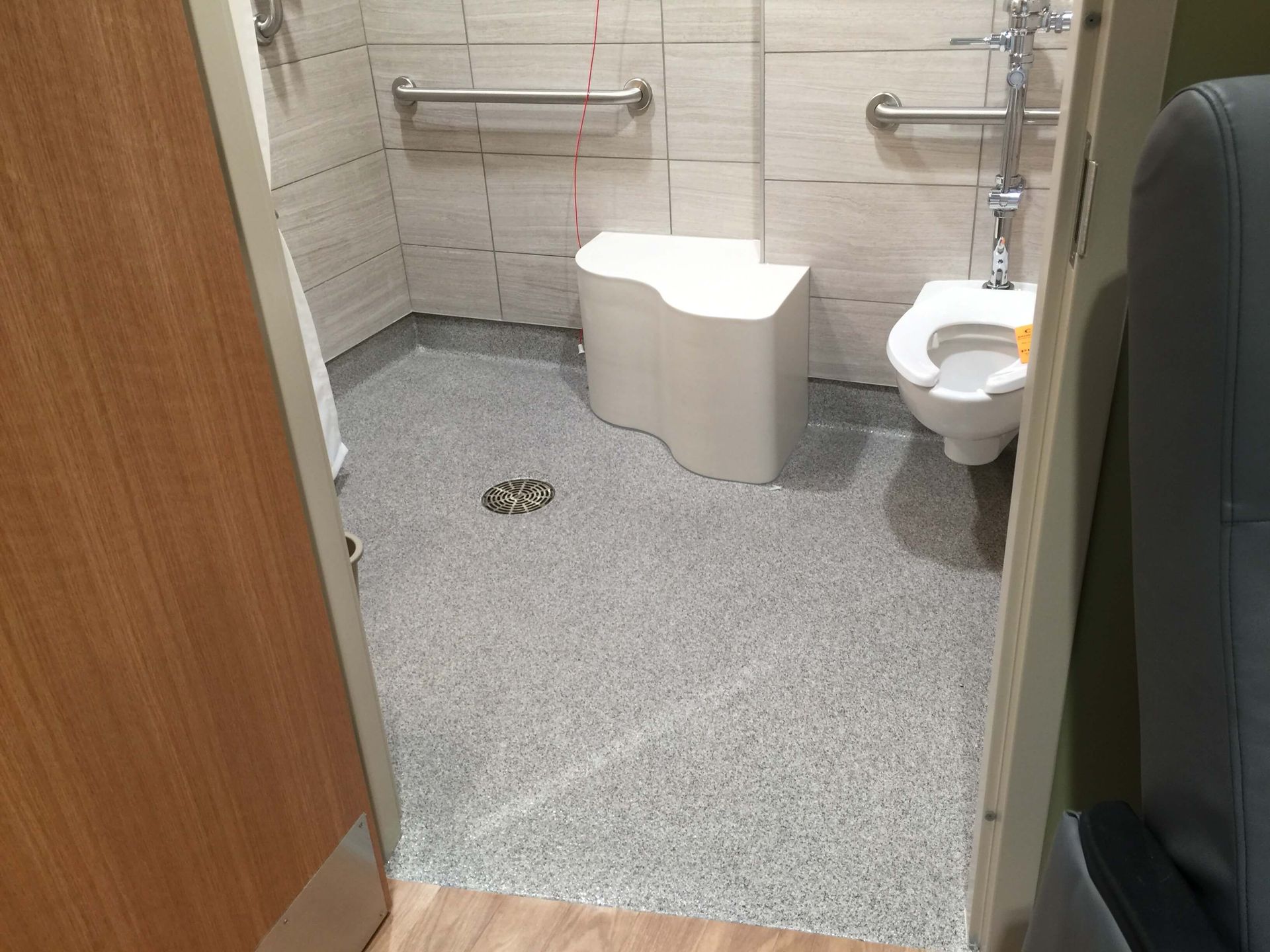 A bathroom with a toilet , shower , and bench.