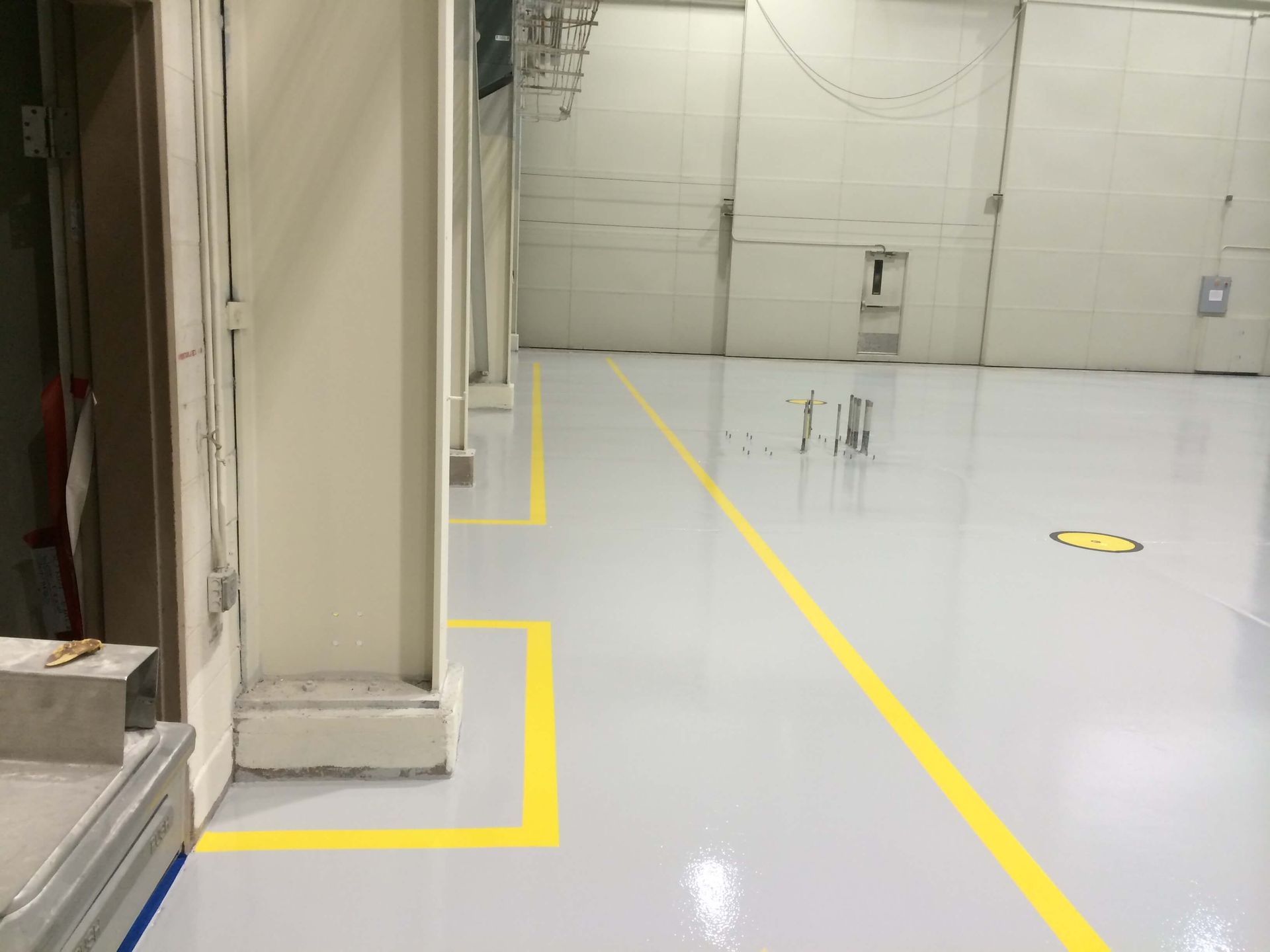 Large, empty industrial room with a shiny, light gray floor and yellow painted lines.