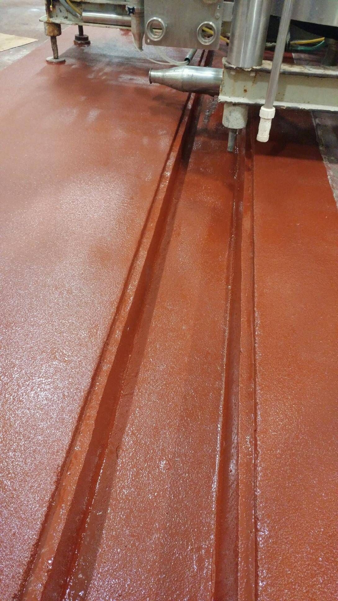 A waterjet cutting machine in operation, carving parallel grooves into a red surface.