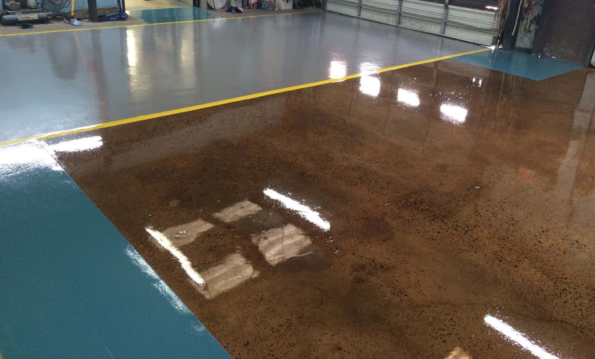 Brown, gray, and teal epoxy-coated concrete floor with yellow line in an industrial setting.
