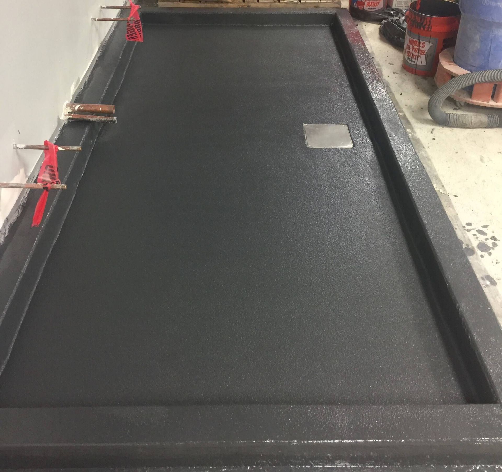 Newly constructed shower base, gray waterproof coating, drain visible, construction tools present.