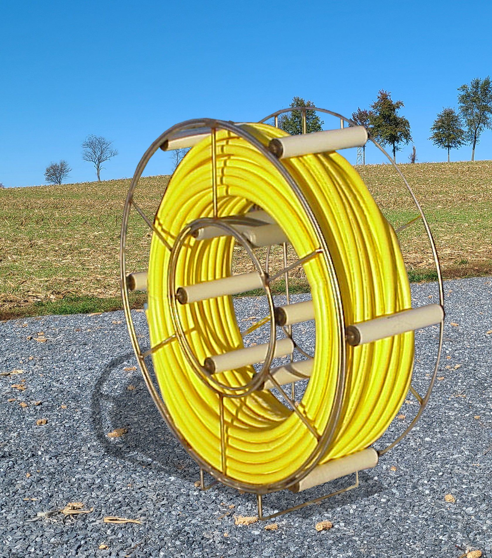 A spool of yellow hose is sitting on a gravel road