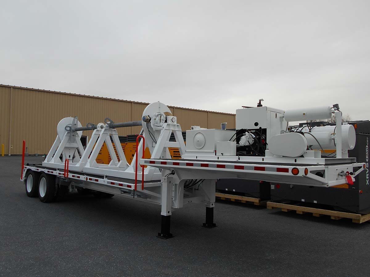 A trailer with a machine on it is parked in front of a building.