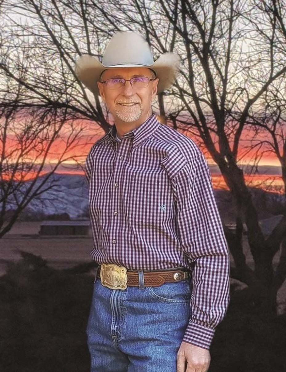 A man wearing a cowboy hat and plaid shirt is standing in front of a sunset.