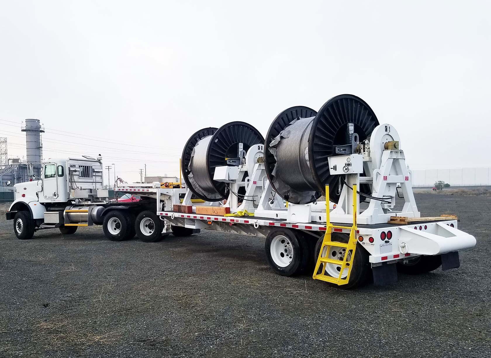 A truck is pulling a trailer with a bunch of spools on it.