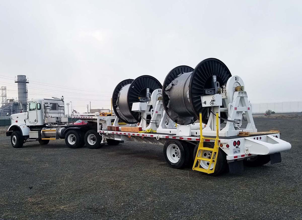 A semi truck is pulling a trailer with large spools of wires on it.
