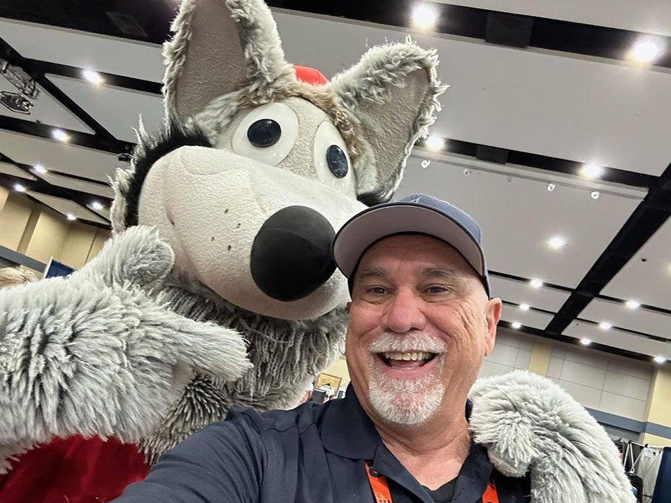 A man is taking a selfie with a stuffed wolf mascot.