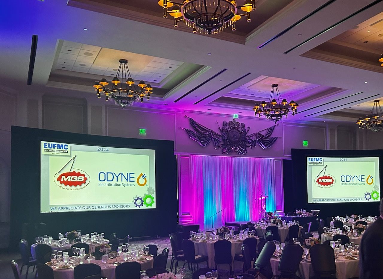 A large room with tables and chairs and two large screens.