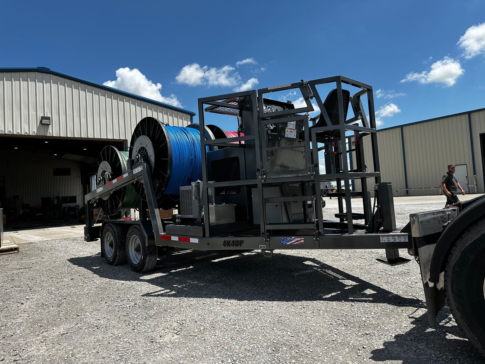 A trailer with a machine on it is parked in front of a building.