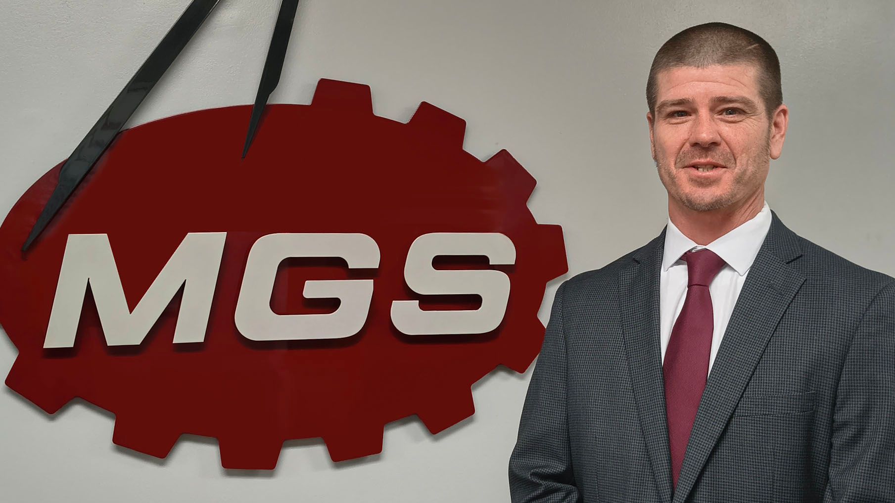 Man in suit stands in front of a red gear logo with 