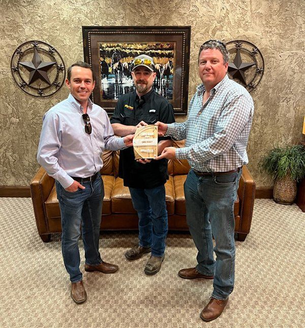 Three men are standing in front of a couch holding a piece of wood.