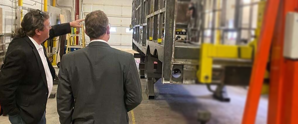 Two men in suits are standing in a factory looking at a machine.