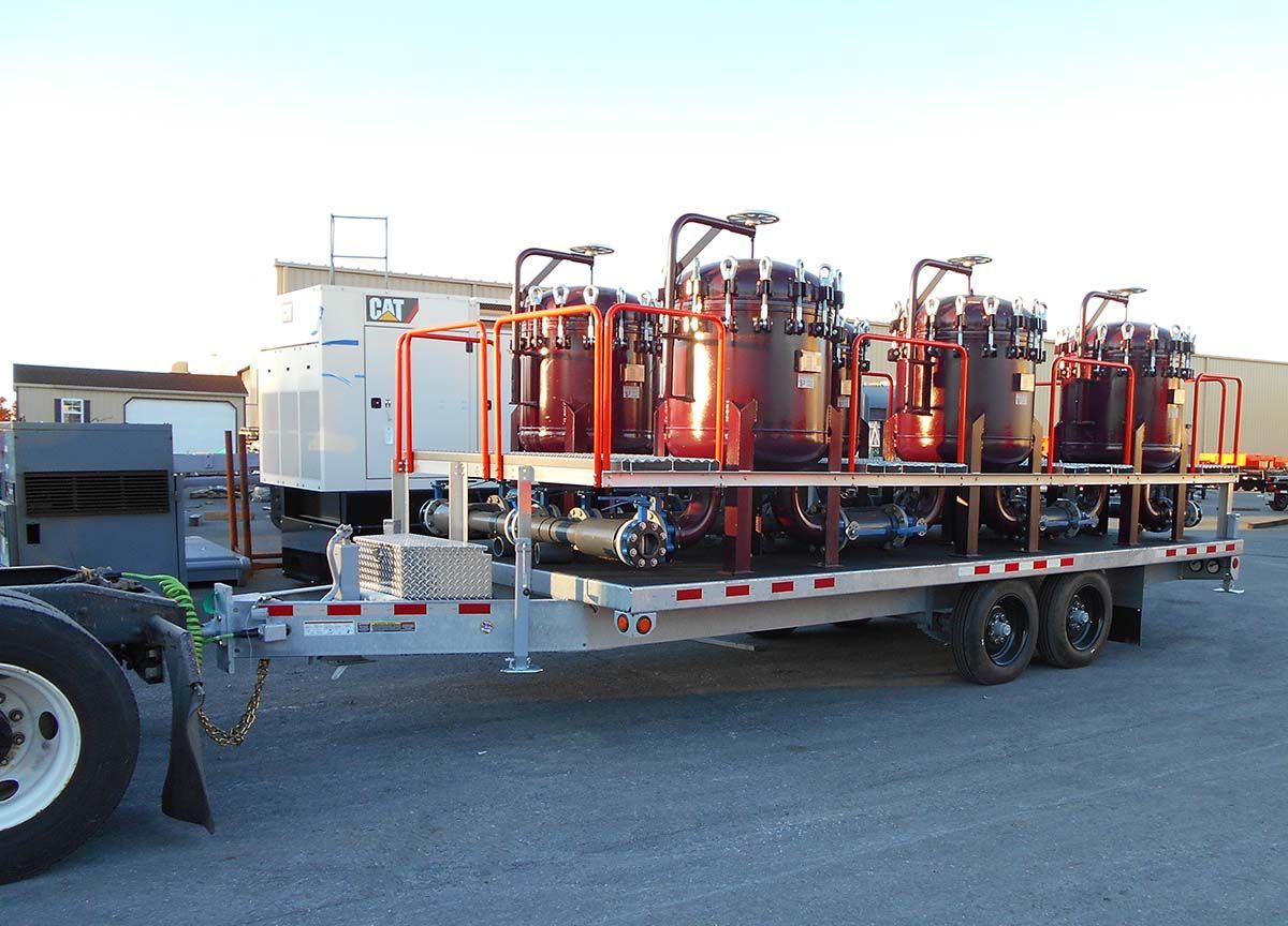 A trailer with a lot of machinery on it is parked next to a truck.