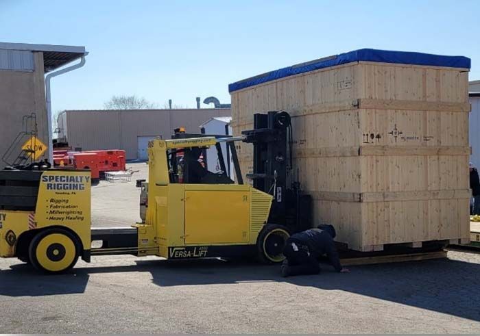A yellow forklift is carrying a large wooden box