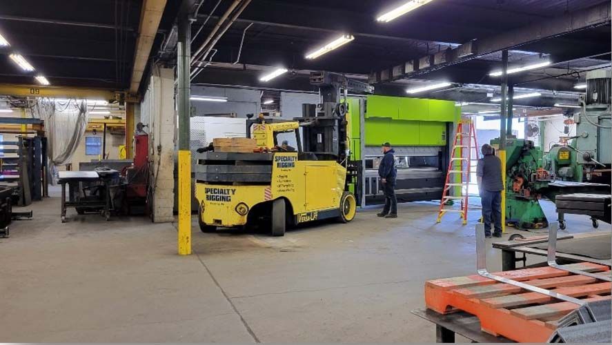 A yellow forklift is moving a large piece of metal in a factory.