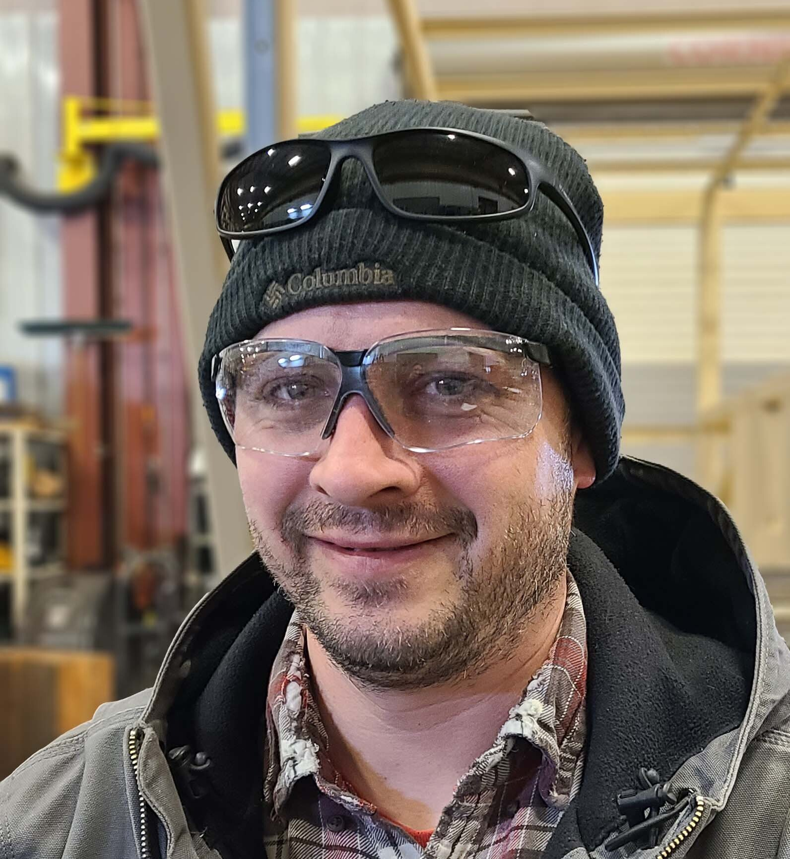 A man wearing a beanie and sunglasses is smiling for the camera.