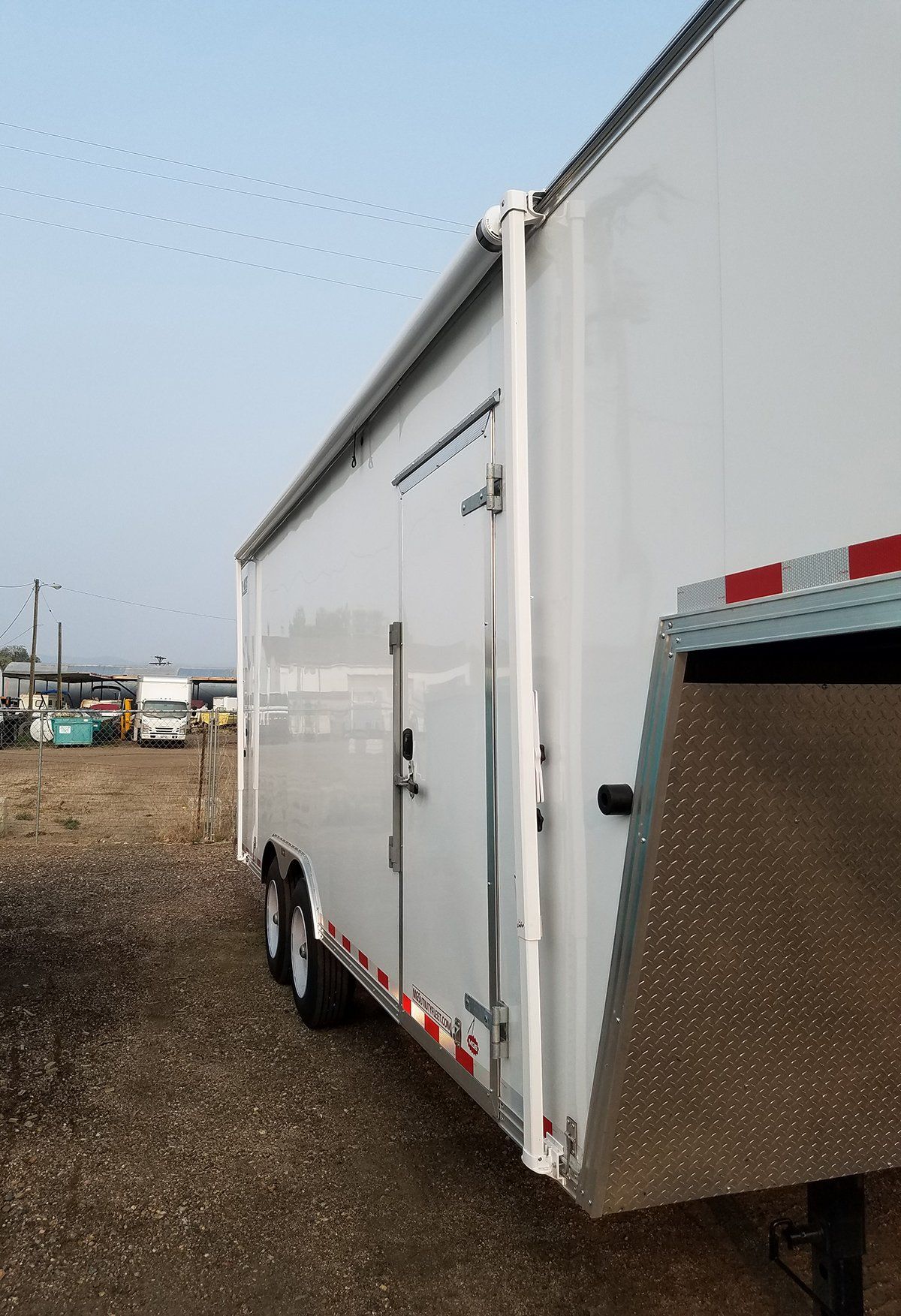 A white trailer is parked in a gravel lot.