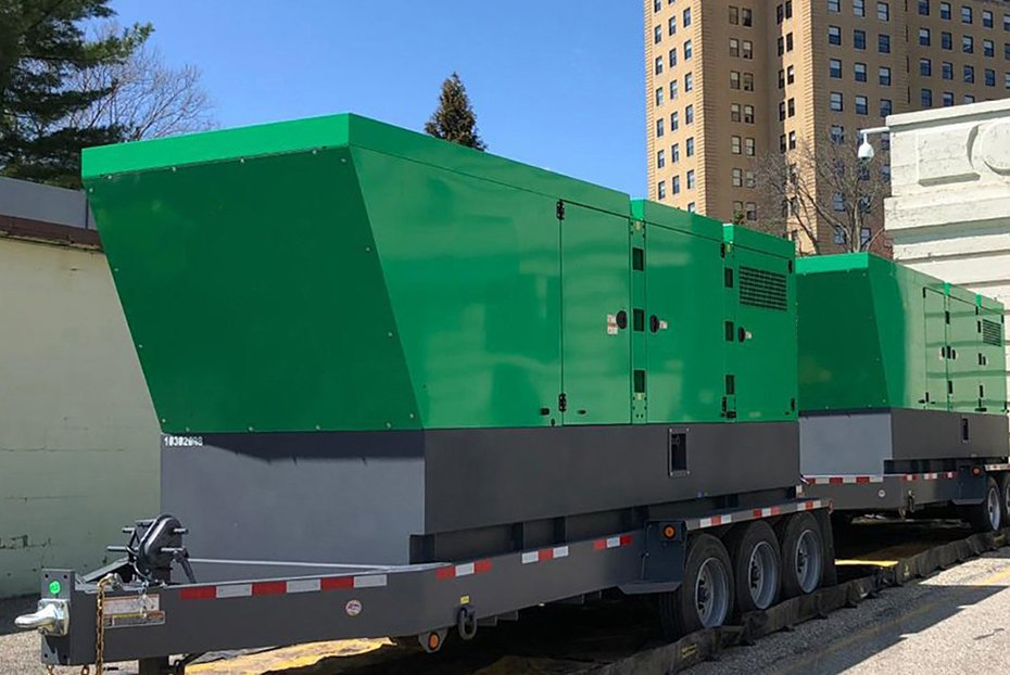 A trailer with two green generators on it is parked in front of a building.