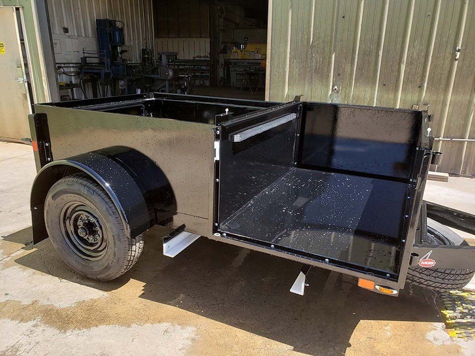 A black trailer with the door open is parked in front of a building.