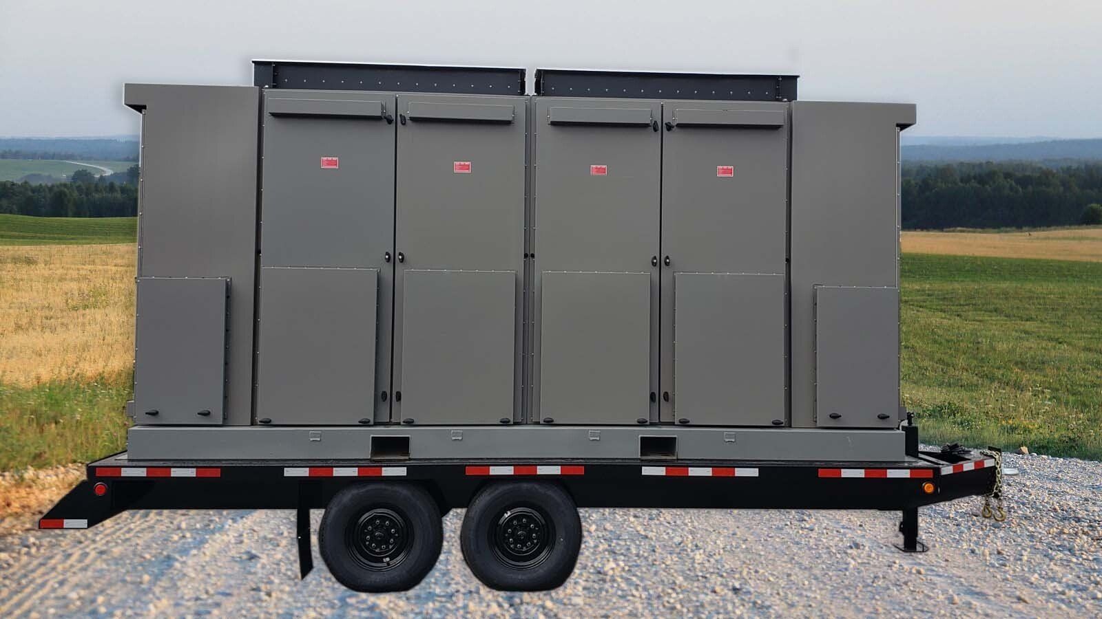 A trailer with a large gray box on it is parked in a field.