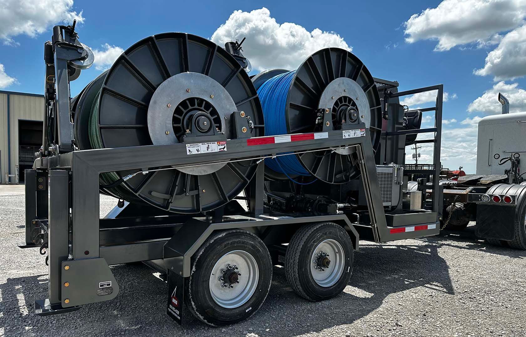 A trailer with two spools of hose on it is parked next to a truck.