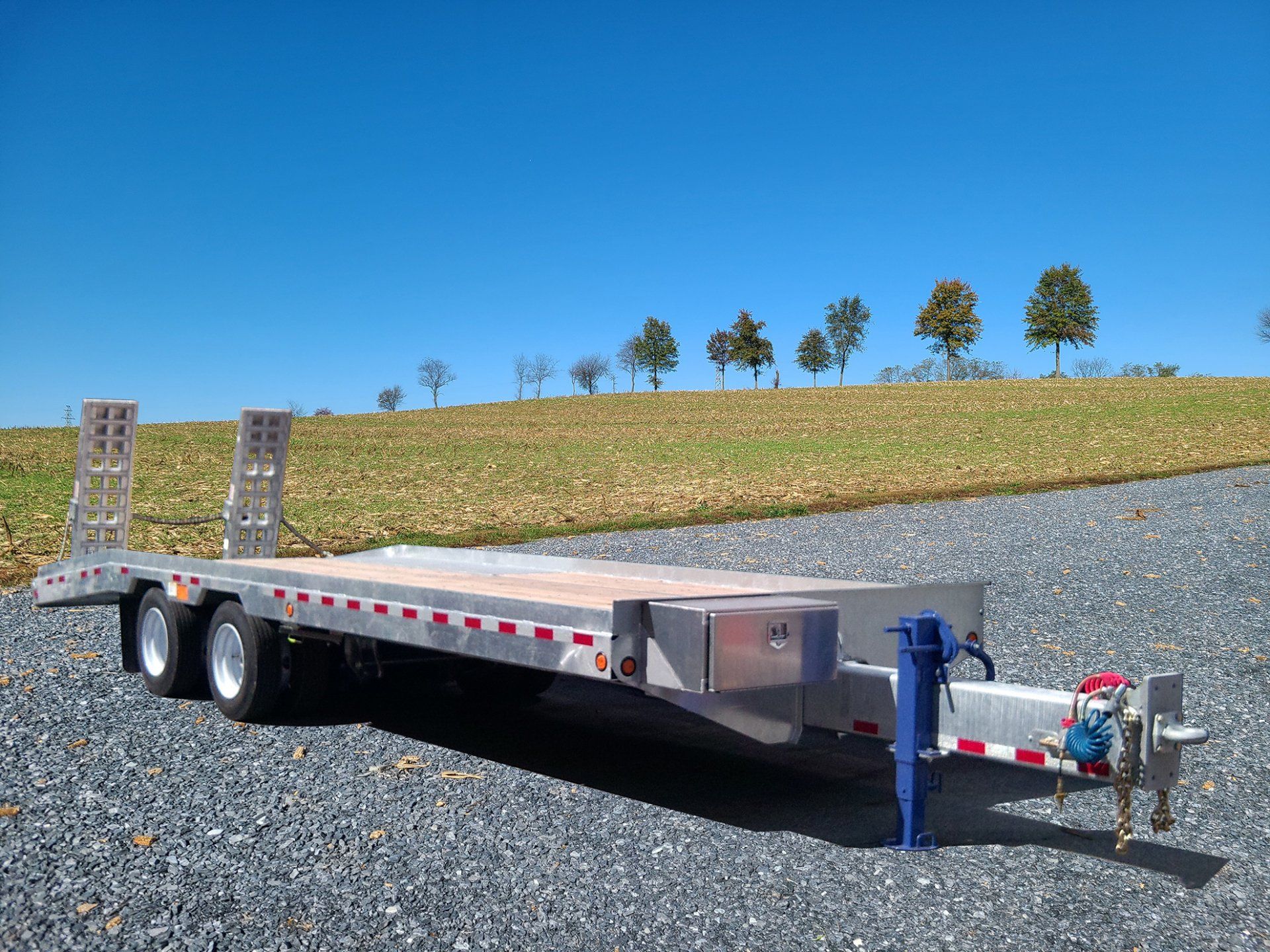 A trailer is parked on a gravel road in front of a field.