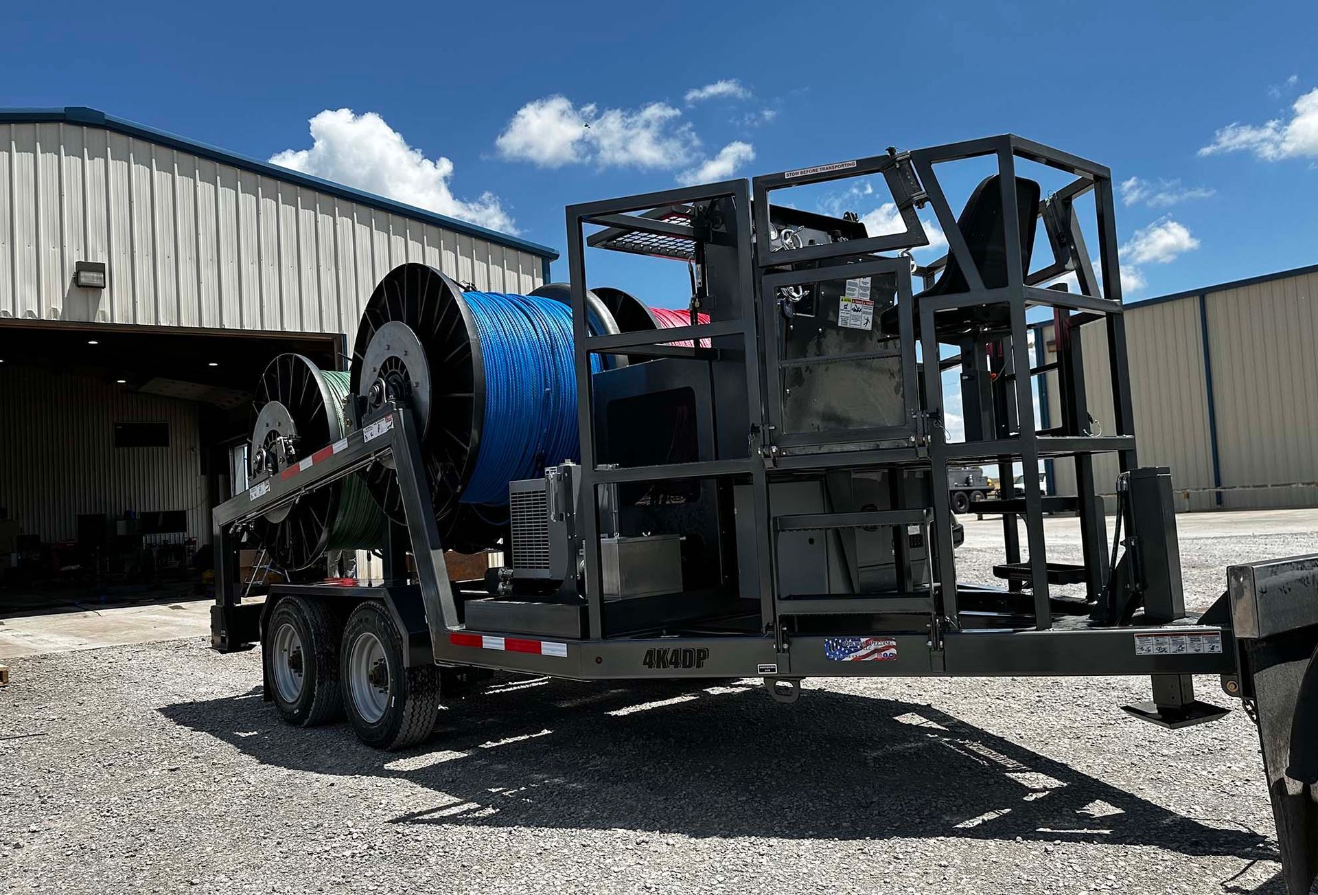 A trailer with a machine on it is parked in front of a building.