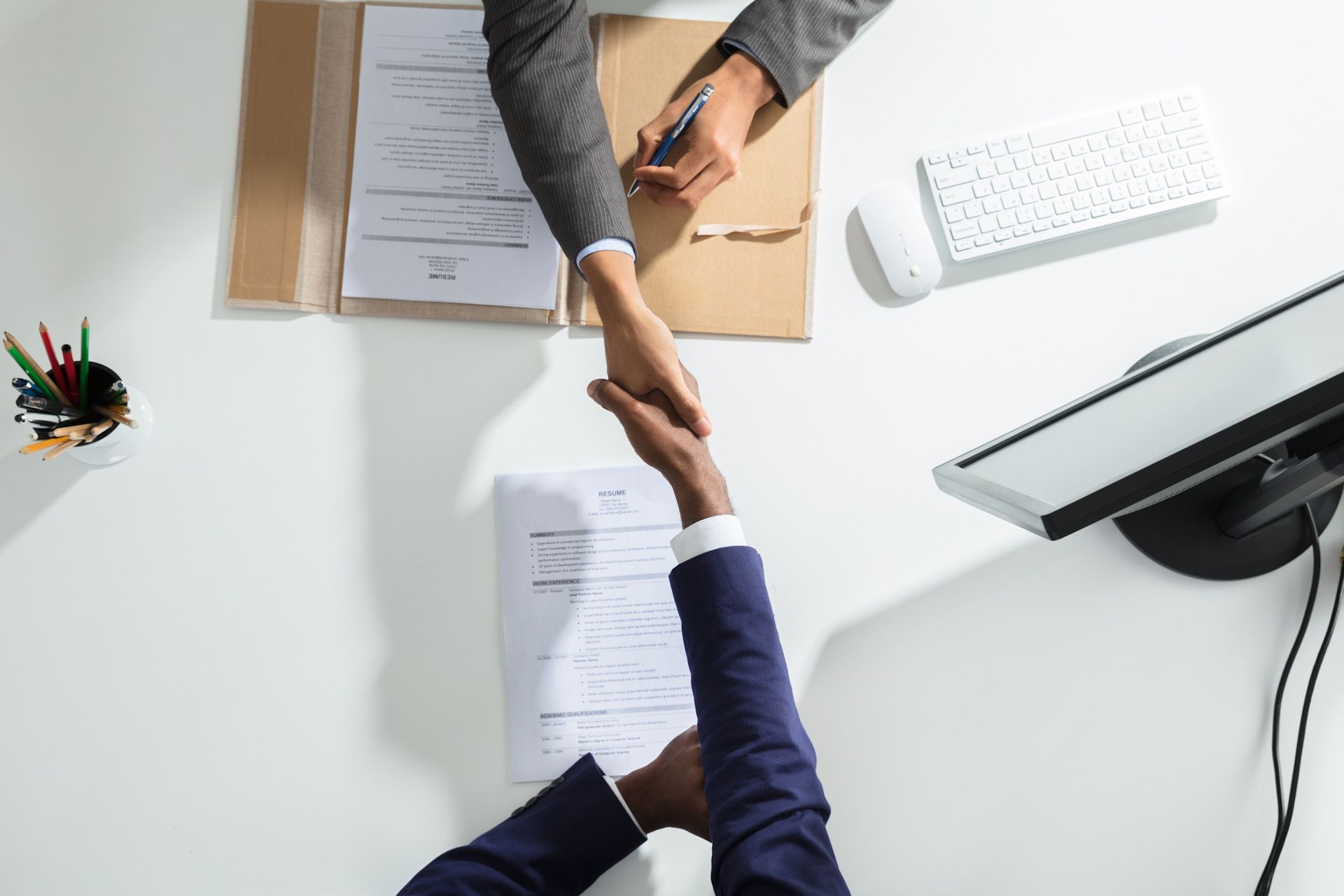 A man and a woman are shaking hands over a desk.